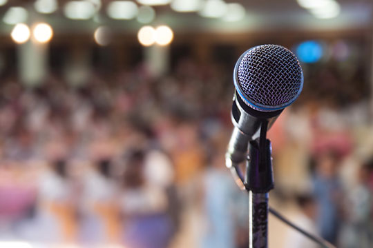 A microphone stand on a stage in front of an audience.