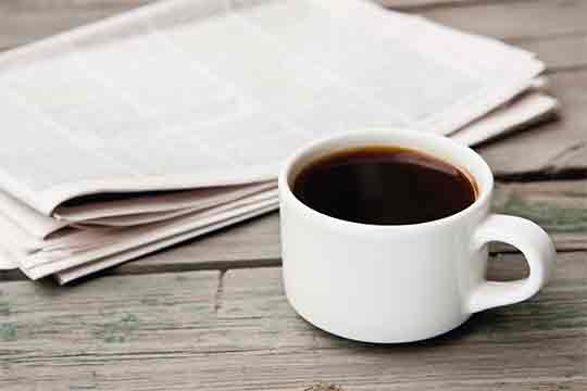 A newspaper and a cup of coffee on a table.