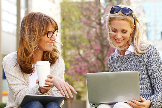 Businesswomen sitting at office park while using digital tablet and laptop