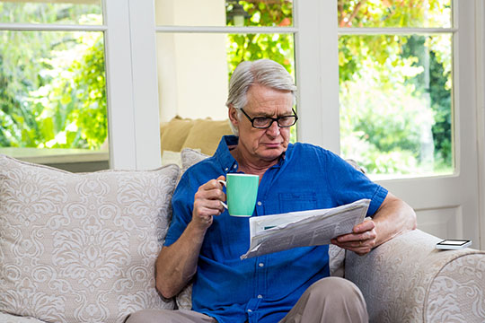 A man reading a newspaper while having coffee in living room at home.