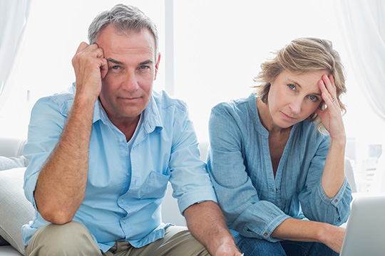 A couple sitting on a couch looking stressed