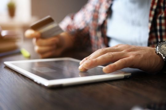 Homme adulte tenant un téléphone intelligent et une carte de crédit.