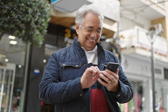 Smiling adult man outdoors using smartphone.
