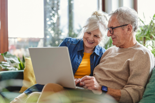 Adult couple using laptop while resting on sofa at home.