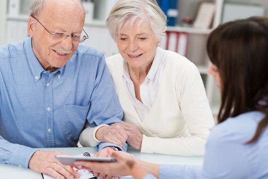 Smiling elderly couple receiving financial advice from a female broker who is showing them a calculator.