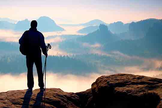 Hiker on rocky view point above misty valley.