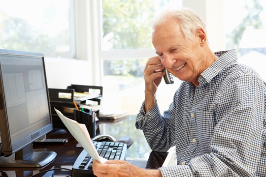 A man on a phone in front of desktop computer.