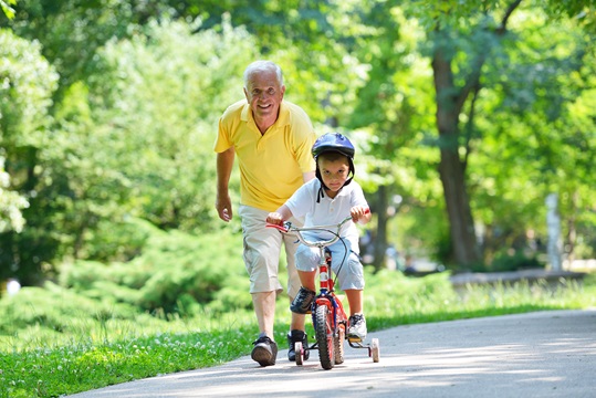 Un grand-père heureux marchant à côté avec le petit-fils sur un vélo