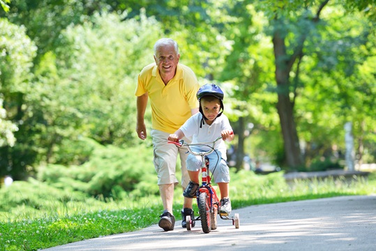 A happy grandfather walking alongside with grand child on a bicycle.