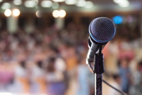 A microphone stand on a stage in front of an audience. A microphone stand on a stage in front of an audience.