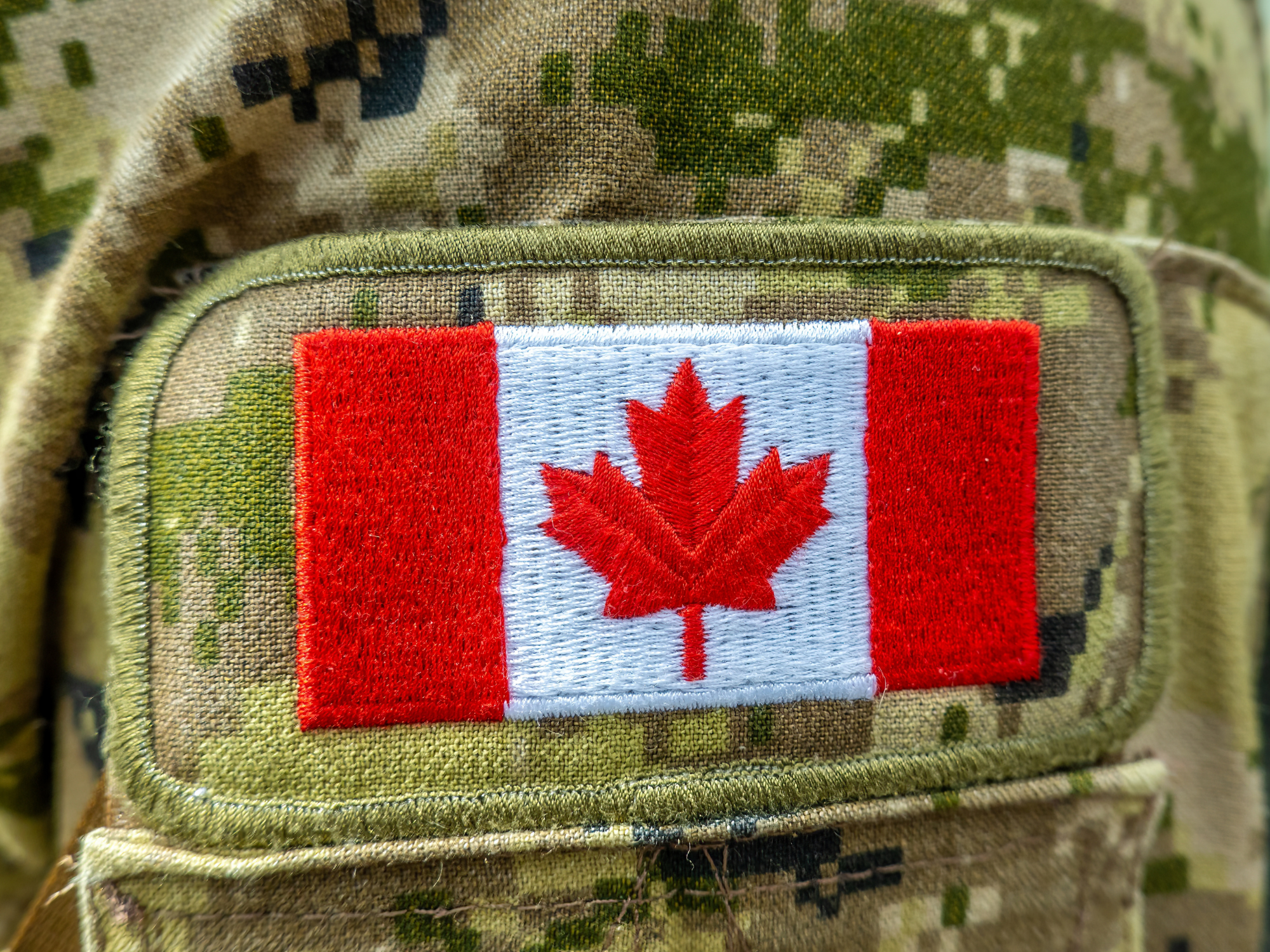Un écusson représentant le drapeau canadien sur un uniforme de camouflage militaire.