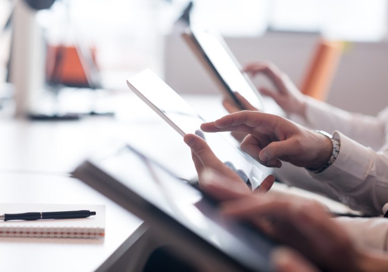 Gros plan sur les mains des membres de l’équipe tenant des tablettes et travaillant à un bureau.