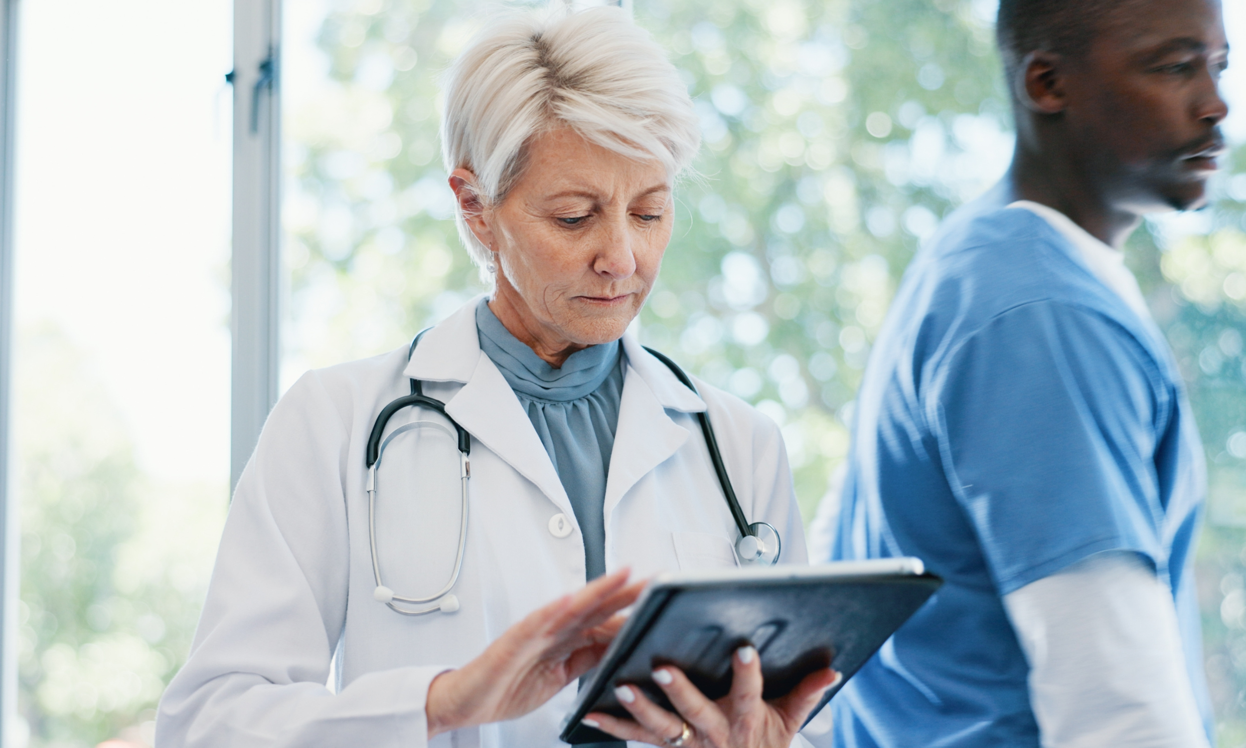 Une médecin[AJ7.1] consulte des informations sur une tablette dans un milieu de soins de santé.