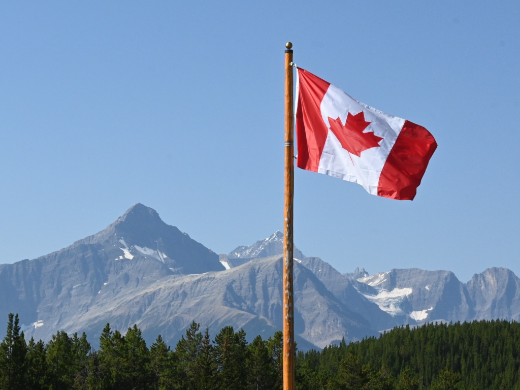 Drapeau Canadien flottant au premier plan d’un paysage montagneux.