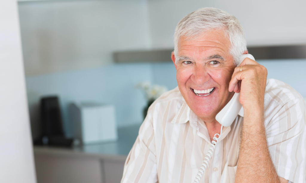 Un homme adulte sourit en conversant sur téléphone filaire blanc.